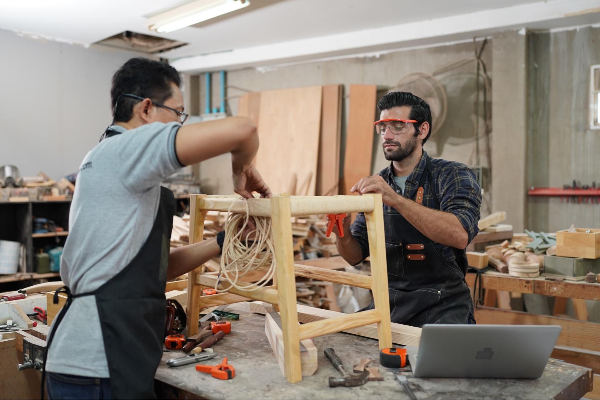 "Dos carpinteros armando una silla personalizada en el taller de Jocholá Muebles, destacando trabajo artesanal y precisión."
